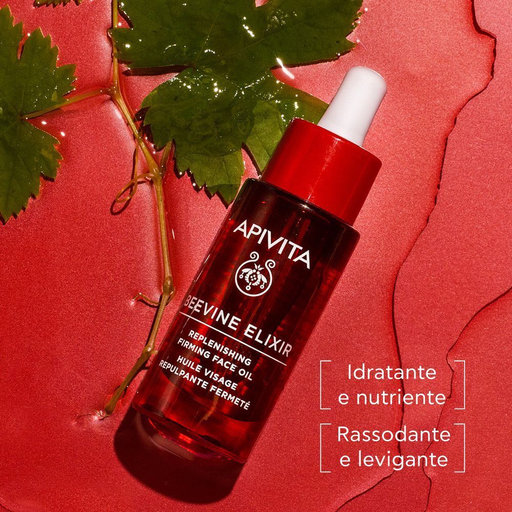 Olio Viso Apivita Beevine Elixir in flacone di vetro rosso con contagocce, circondato da acqua e foglie di vite.
