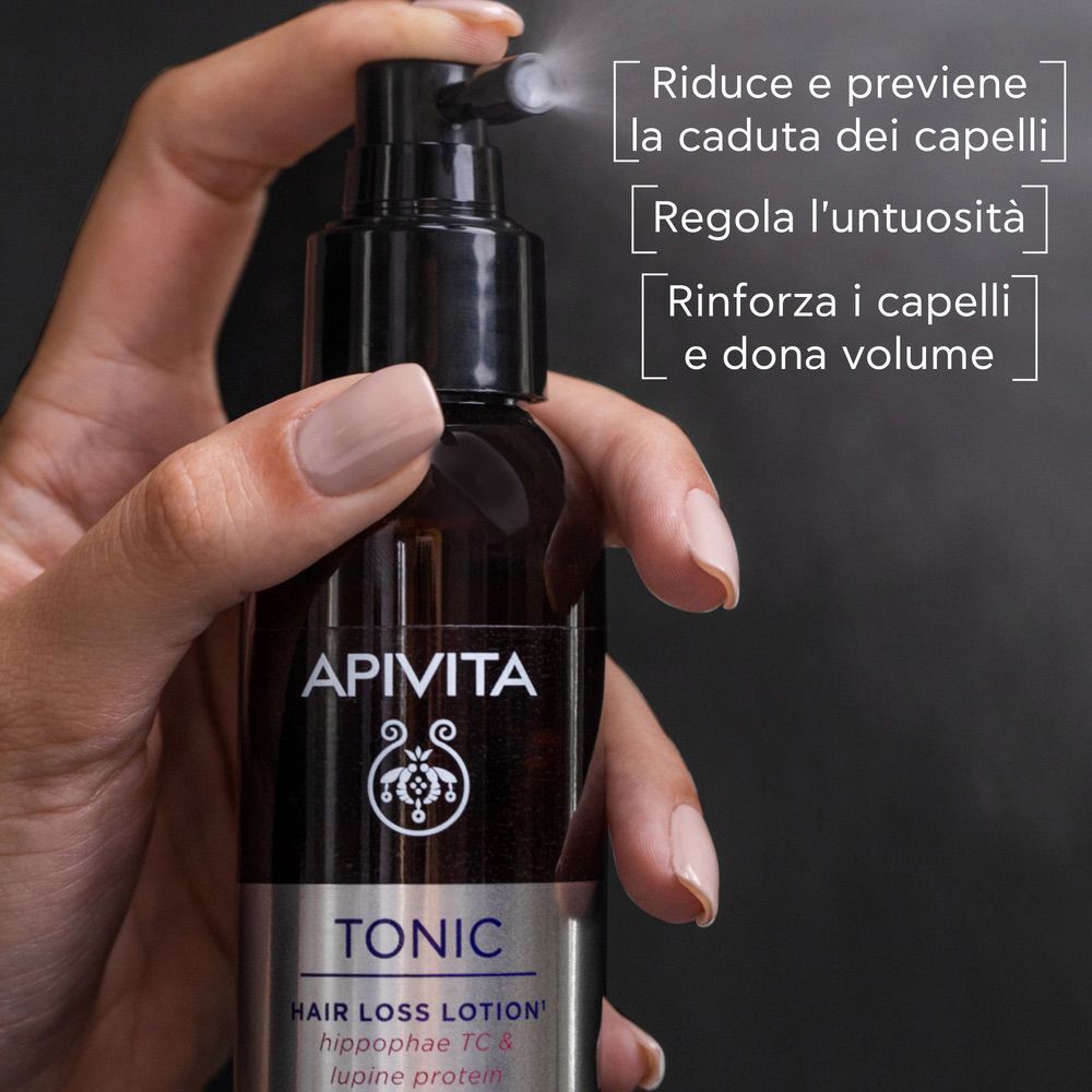 Mano che tiene un flacone di lozione APIVITA TONIC. Testo: Riduce e previene la caduta dei capelli.