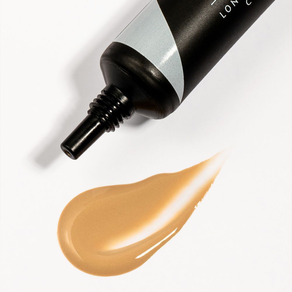 Una goccia di primer color oro-marrone accanto al tubetto aperto.