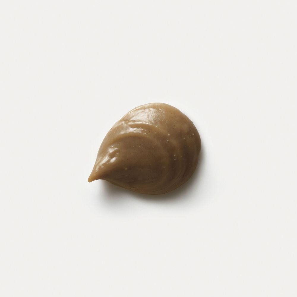Una goccia di crema shampoo color marrone chiaro su sfondo bianco.