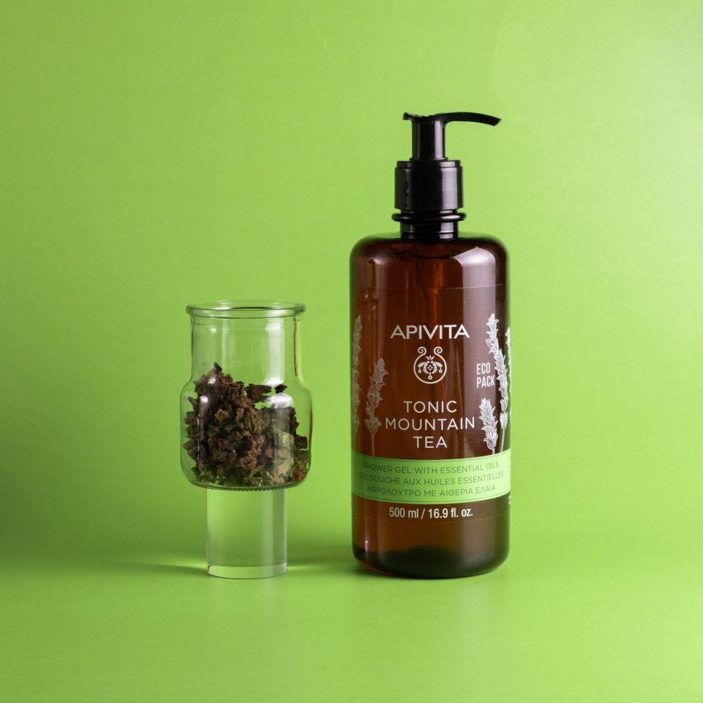 Gel doccia APIVITA TONIC MOUNTAIN TEA accanto a un bicchiere con tè di montagna.