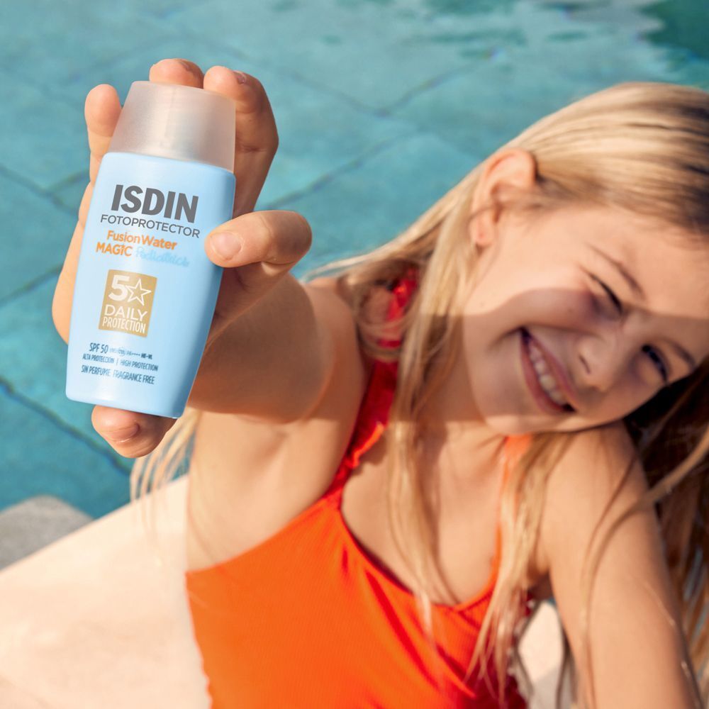 Bambina che tiene in mano un flacone di crema solare ISDIN Fotoprotector Fusion Water Magic Pediatrics vicino alla piscina.