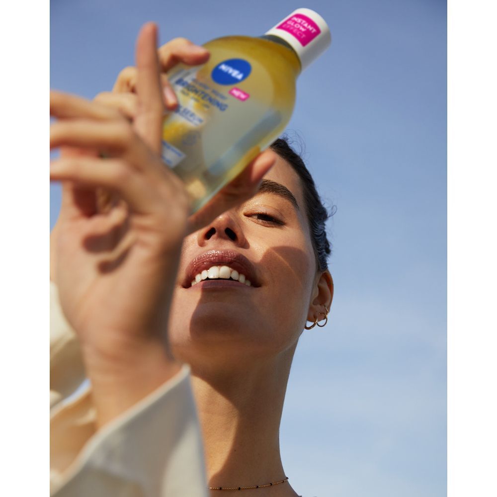 Una donna tiene una bottiglia di acqua micellare Nivea Skin Glow davanti al viso.