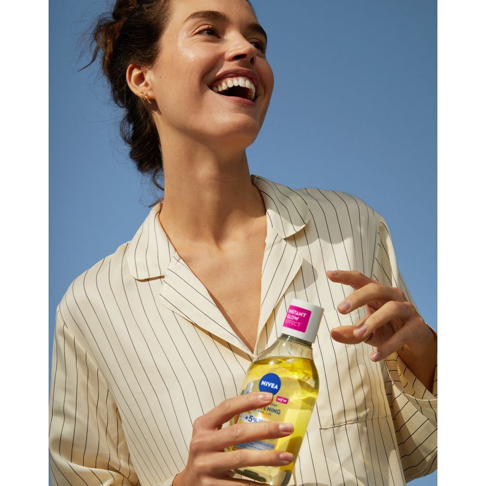 Una donna sorridente tiene una bottiglia di acqua micellare Nivea Skin Glow.