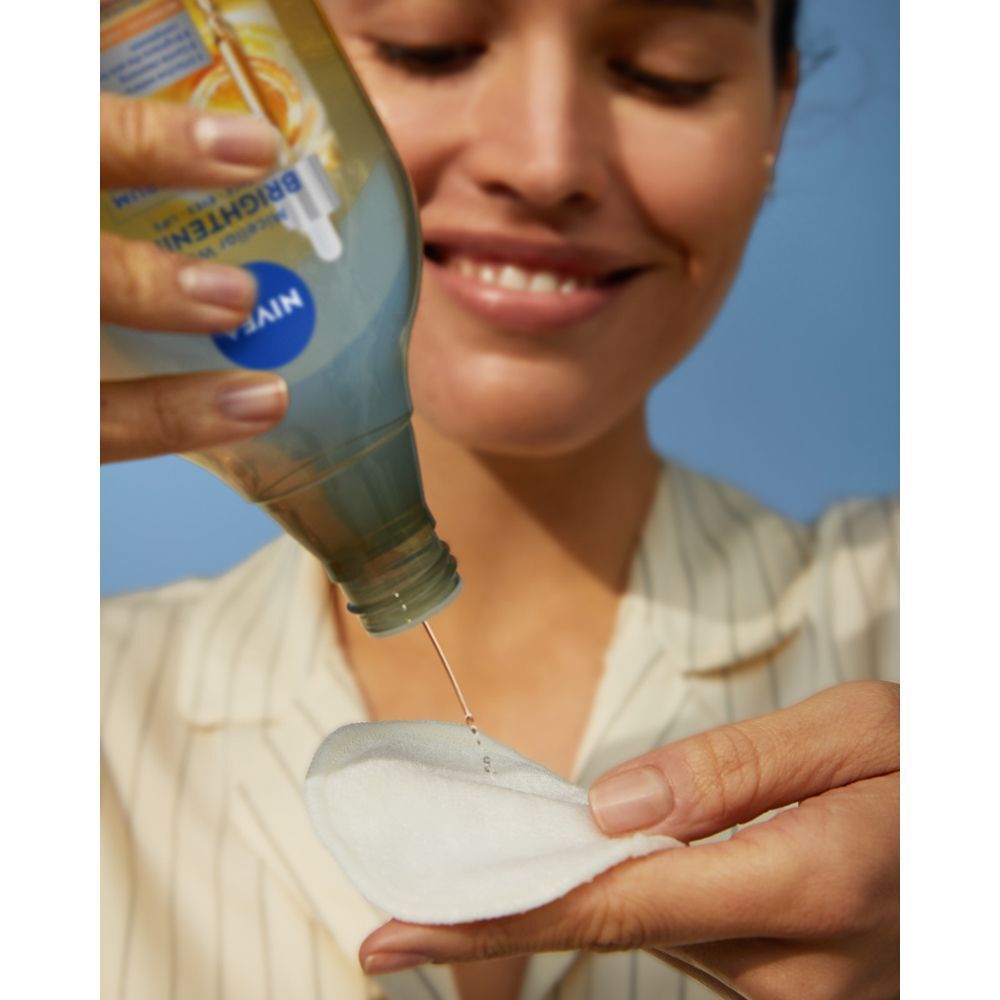 Una donna versa Nivea Acqua Micellare Skin Glow su un dischetto di cotone.