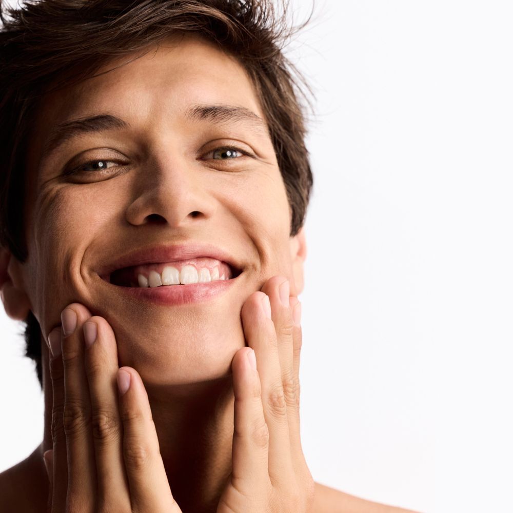 Un uomo sorridente si tocca il viso con entrambe le mani.