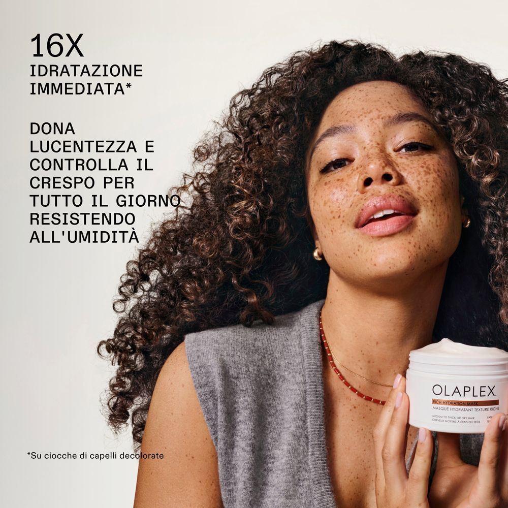 Donna con capelli ricci tiene un barattolo Olaplex Rich Hydration Mask. Idratazione immediata.