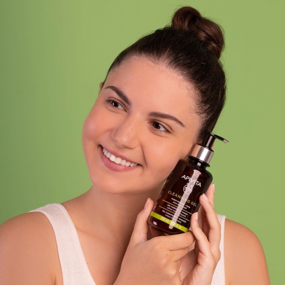 Una donna tiene in mano un flacone di Gel Purificante APIVITA con erogatore.