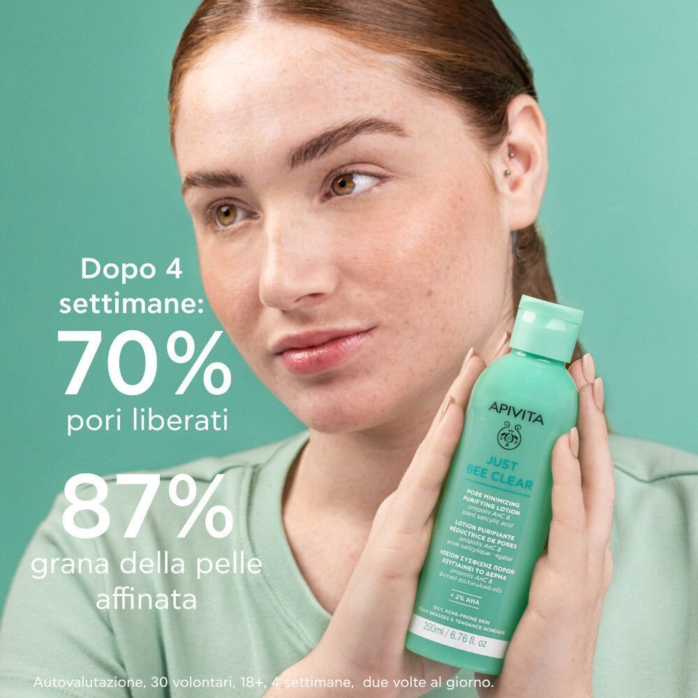 Donna tiene una bottiglia di lozione Apivita Just Bee Clear. Testo: 'Dopo 4 settimane: 70% pori liberati, 87% grana della pelle affinata'.