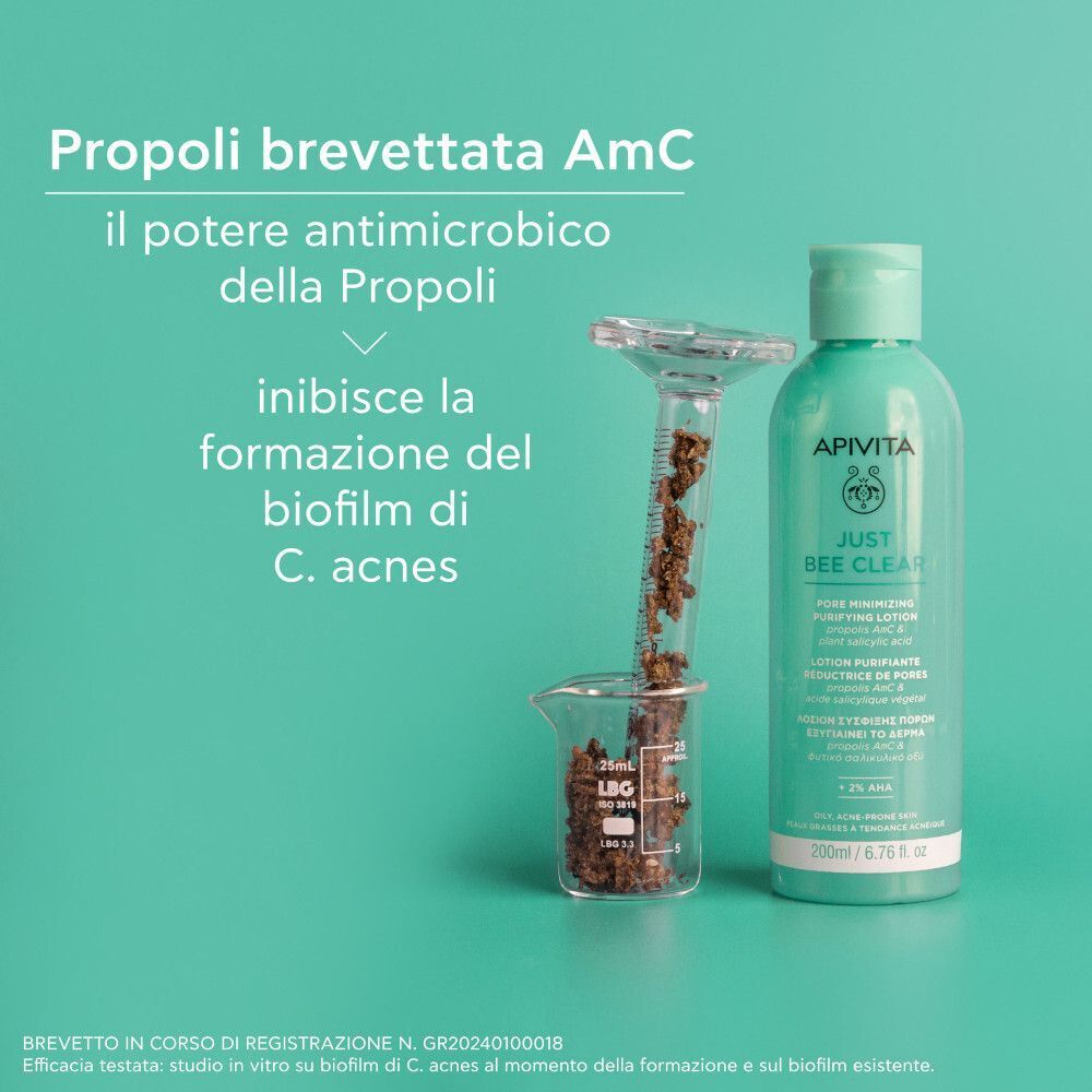 Lozione purificante Apivita Just Bee Clear vicino a strumenti di laboratorio con propoli. Testo: 'Propoli brevettata AmC, il potere antimicrobico'.