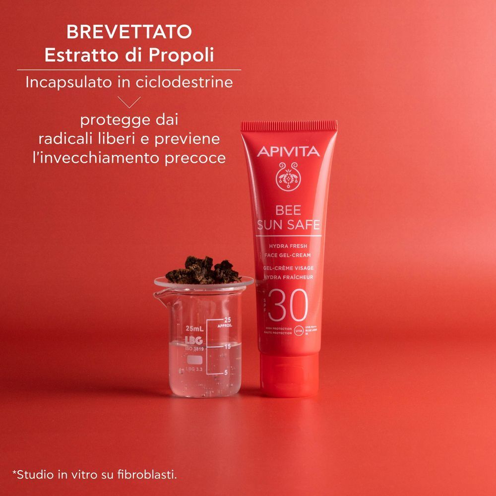Tubo rosso APIVITA Bee Sun Safe Hydra Fresh Face Gel-Cream SPF 30 accanto a estratto di propoli in un becher.