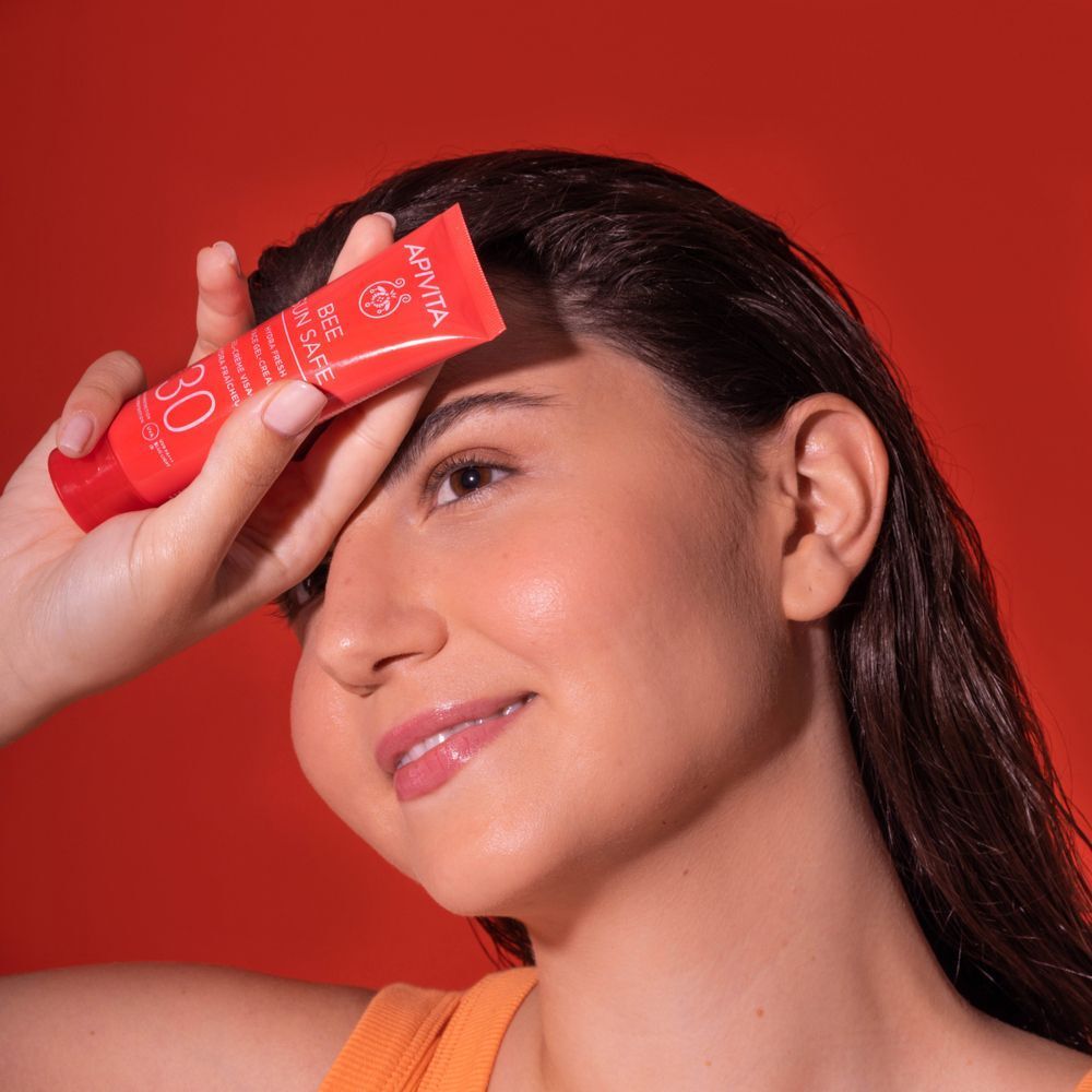 Una donna con in mano un tubetto rosso APIVITA Bee Sun Safe SPF 30, che si copre la fronte.