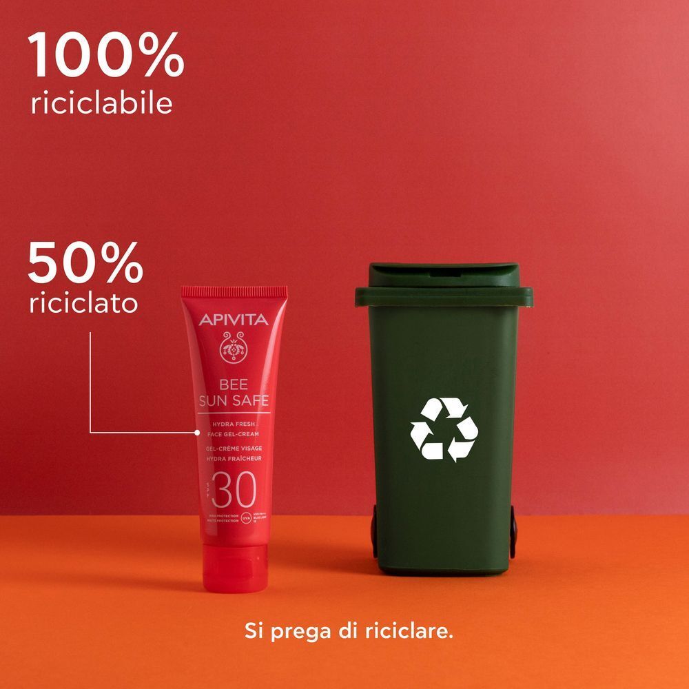 Tubetto rosso APIVITA Bee Sun Safe SPF 30 accanto a un bidone della spazzatura verde con simbolo di riciclo.