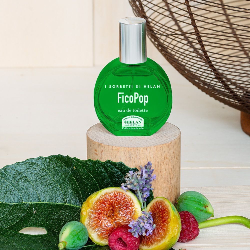 Flacone in vetro verde Eau de Toilette FicoPop su un piedistallo di legno, circondato da fichi e frutti di bosco.