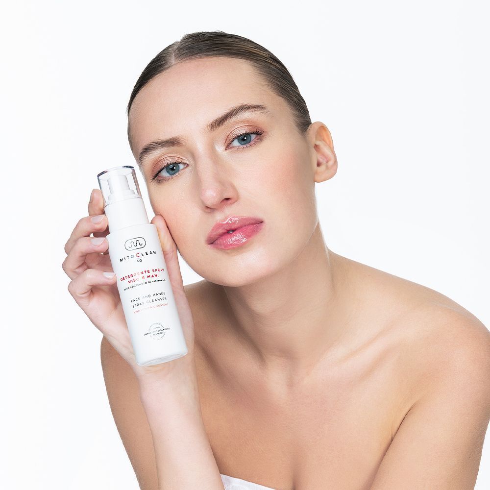 Una donna tiene un flacone spray del detergente viso e mani Mitochon Mitoclean AG.