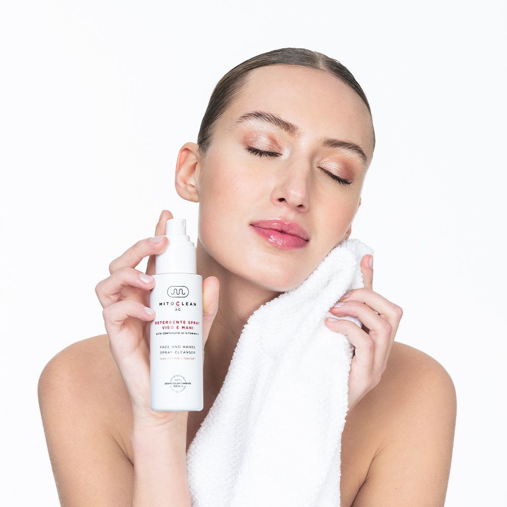 Una donna con gli occhi chiusi tiene in mano un flacone spray di detergente viso e mani Mitochon Mitoclean AG.
