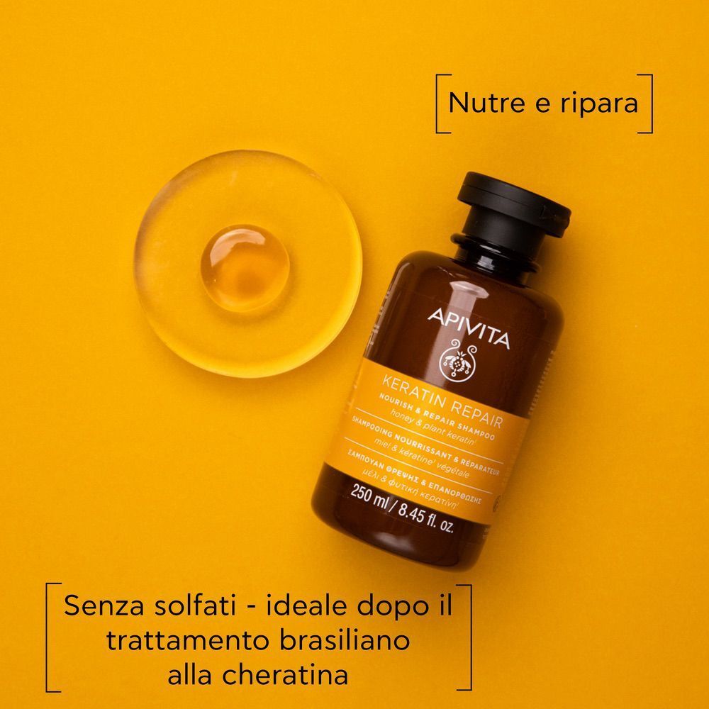 Flacone di shampoo riparatore alla cheratina APIVITA accanto a una goccia di gel su sfondo giallo.