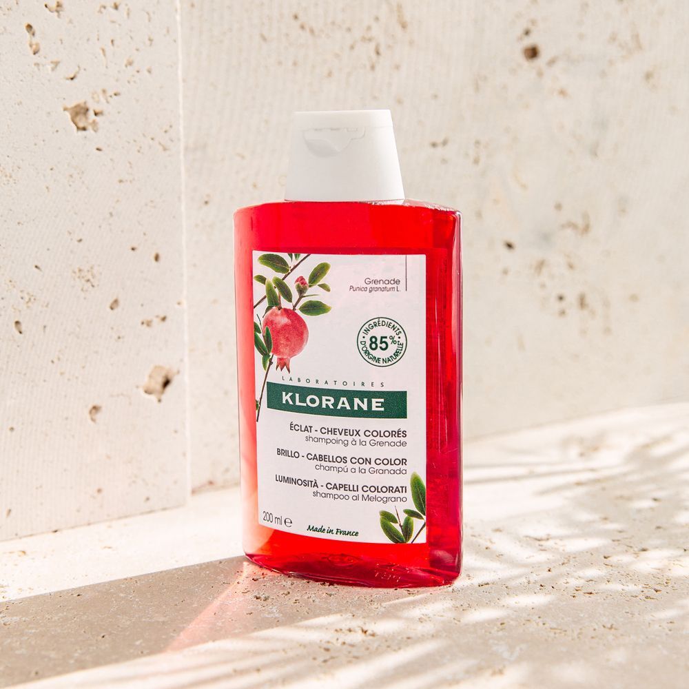 Un flacone di shampoo Klorane con motivo melograno su sfondo chiaro.