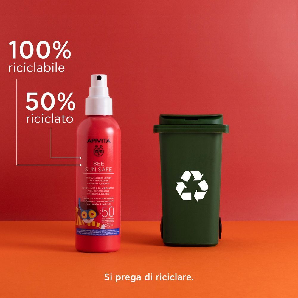 Flacone spray rosso protezione solare SPF 50 accanto a un bidone verde con simbolo di riciclo.