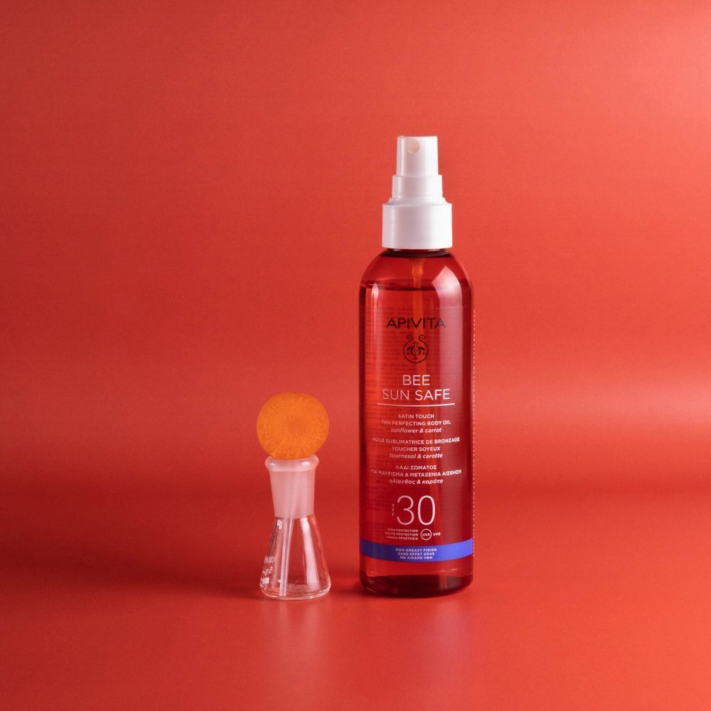 Olio solare APIVITA SPF30 e un piccolo contenitore di vetro con polvere arancione. Sfondo rosso.