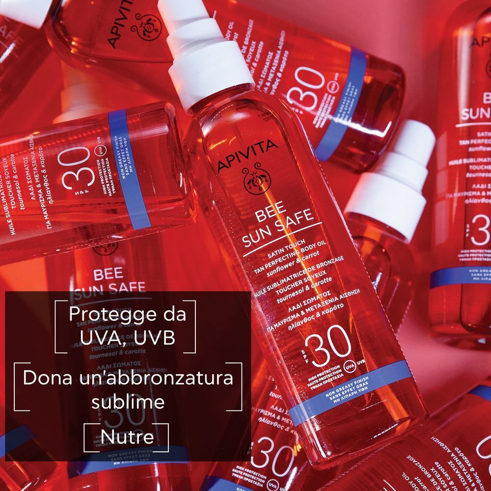 Molti flaconi di olio corpo abbronzante APIVITA SPF30, alcuni a fuoco. Liquido rosso in flaconi trasparenti.