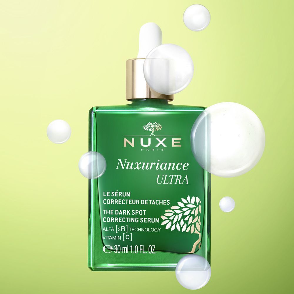 Flacone in vetro verde Nuxe Nuxuriance Ultra siero con bolle su sfondo verde.