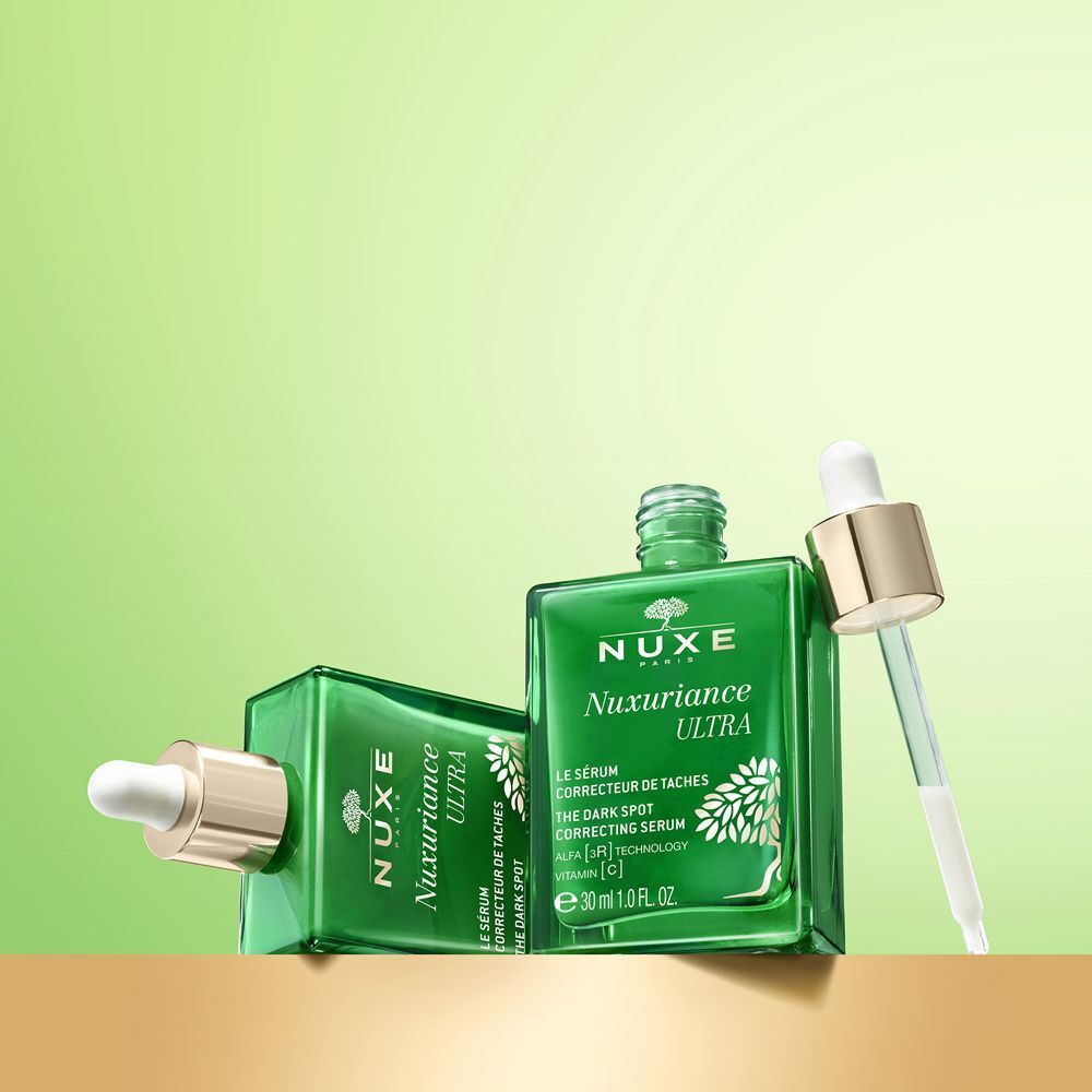 Due flaconi in vetro verde Nuxe Nuxuriance Ultra Siero su piedistallo dorato.