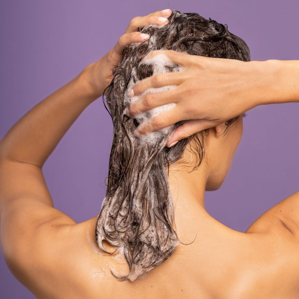 Vista posteriore di una donna che si lava i capelli con shampoo APIVITA Cute Sensibile.