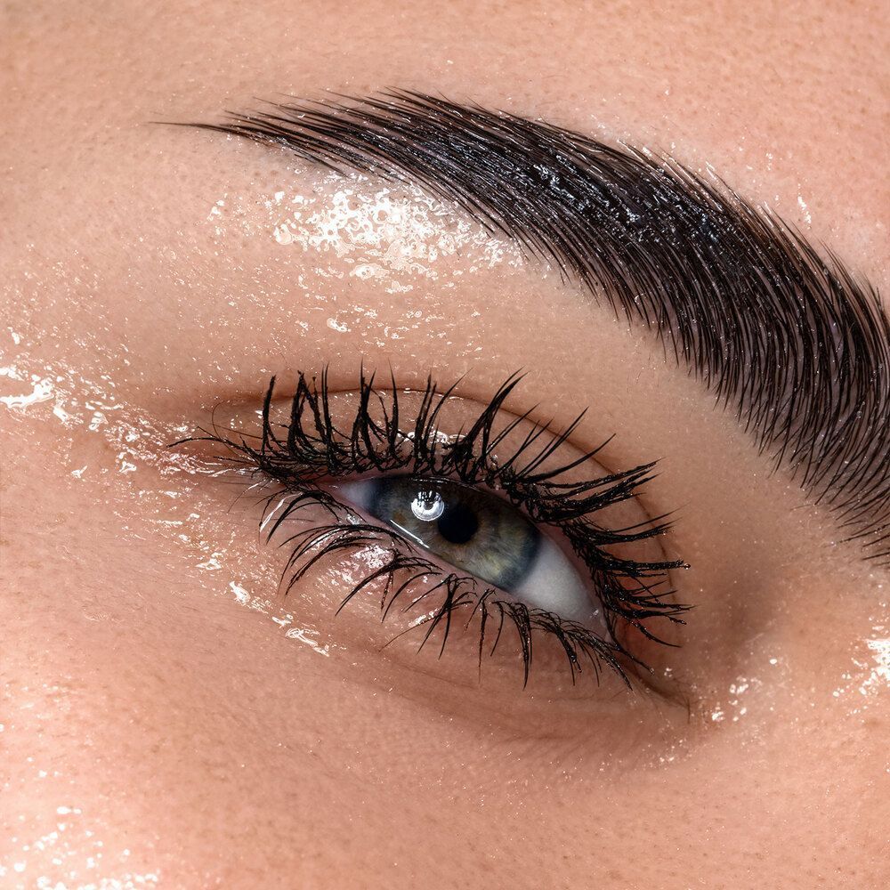 Primo piano di un occhio truccato con mascara Astra The Universal Volume Waterproof, circondato da gocce d'acqua.