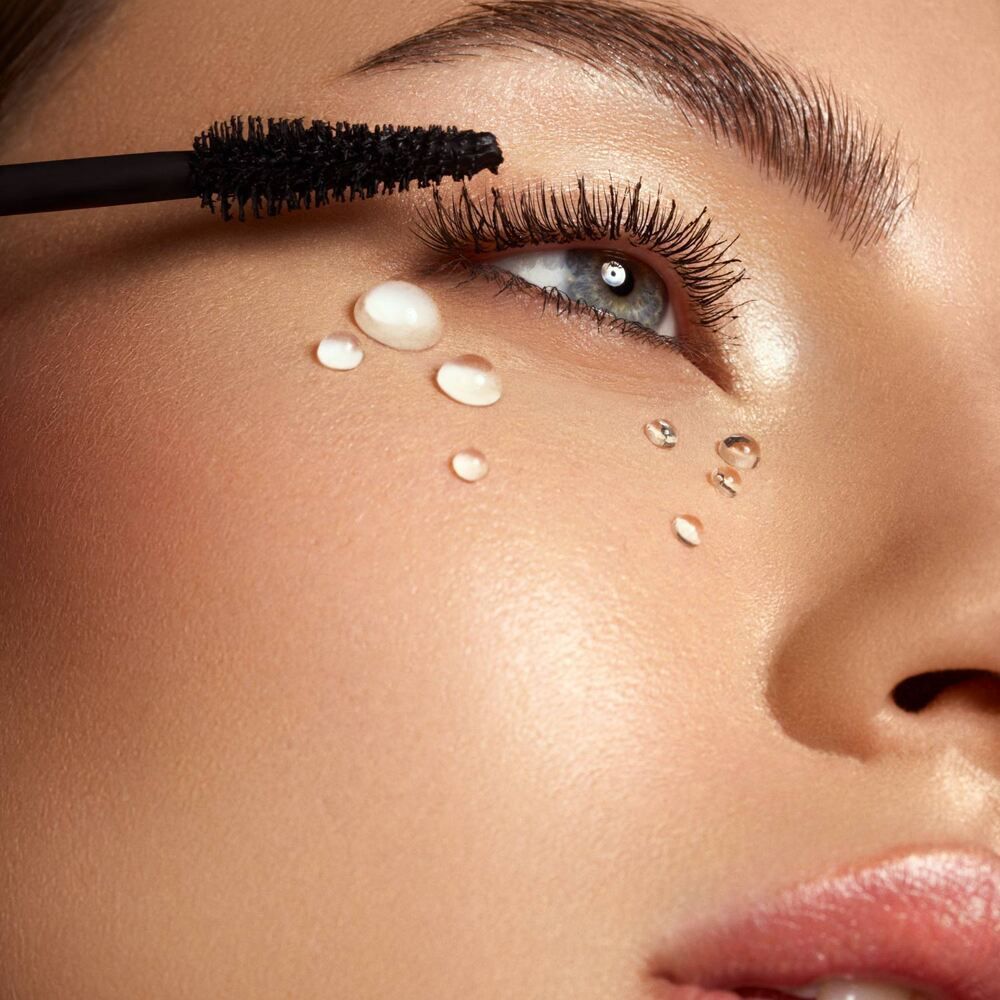 Primo piano di un occhio a cui viene applicato il mascara, con gocce d'acqua sulla guancia.