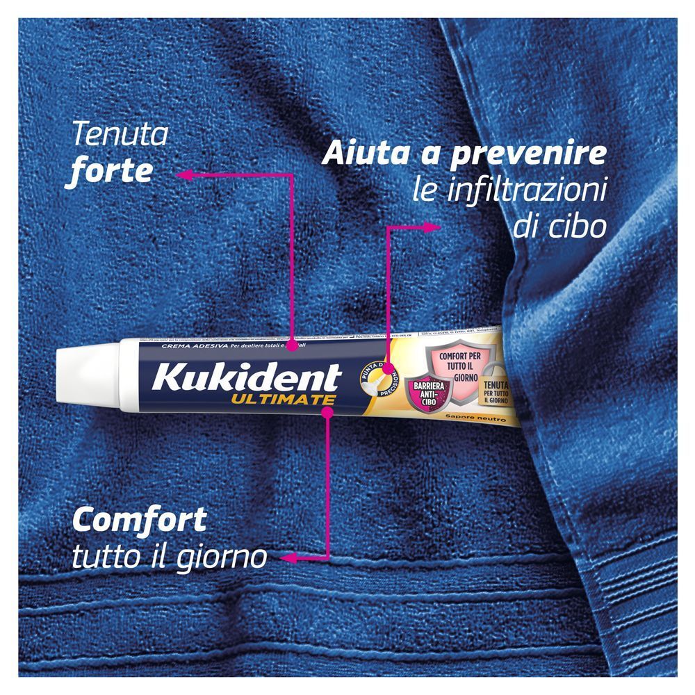 Tubo di crema adesiva Kukident Ultimate appoggiato su un asciugamano blu. Frecce indicano tenuta forte e comfort.