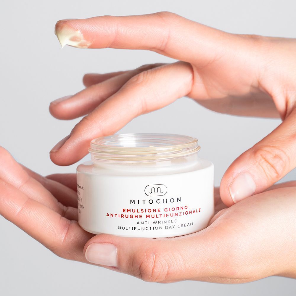 Mani che tengono un vasetto di crema giorno multifunzionale Mitochon con un campione sul dito.