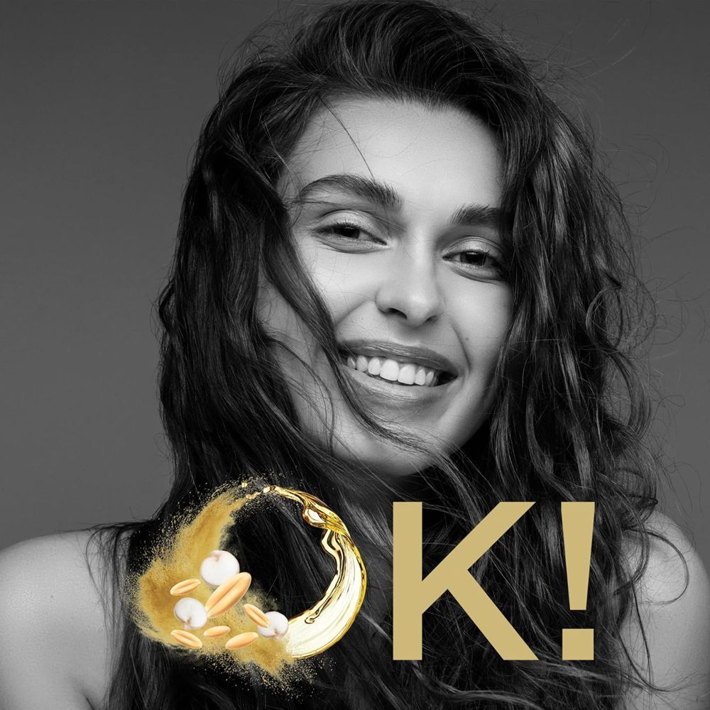Ritratto di donna sorridente con capelli folti, accanto a elementi di cereali e olio e la scritta 'OK!'.
