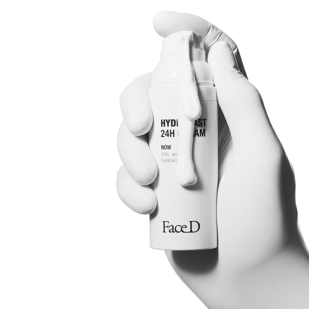 Una mano con guanto bianco tiene un flacone bianco Face D Hydrafast 24H Cream.