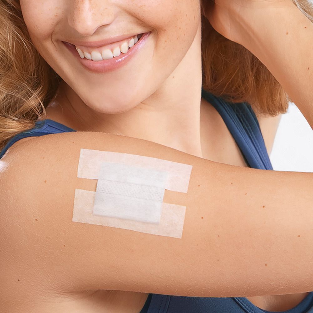 Una medicazione applicata sulla pelle con due strisce adesive bianche e una compressa centrale.
