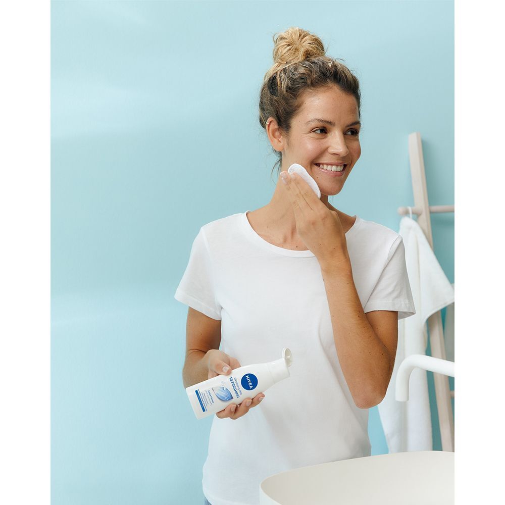 Una donna si pulisce il viso con un dischetto di cotone e latte detergente Nivea in un bagno.