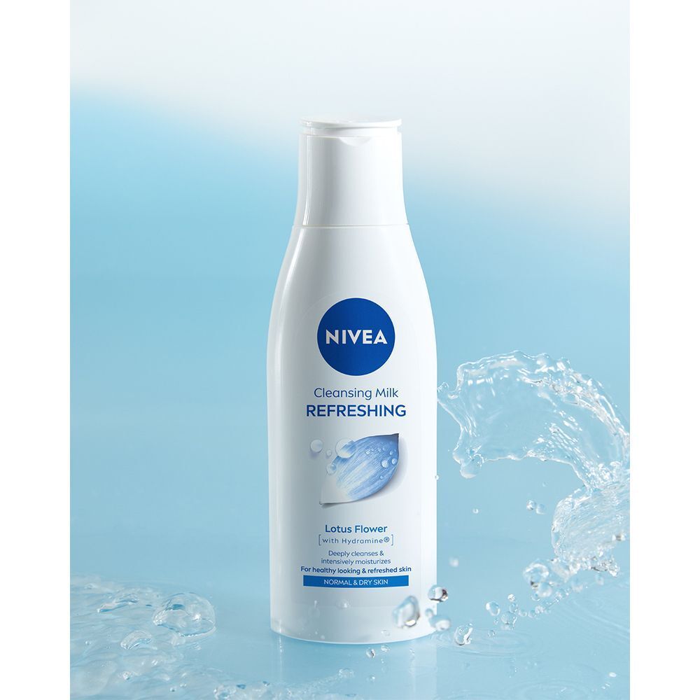 Un flacone bianco Nivea di latte detergente rinfrescante su sfondo blu con schizzi d'acqua.
