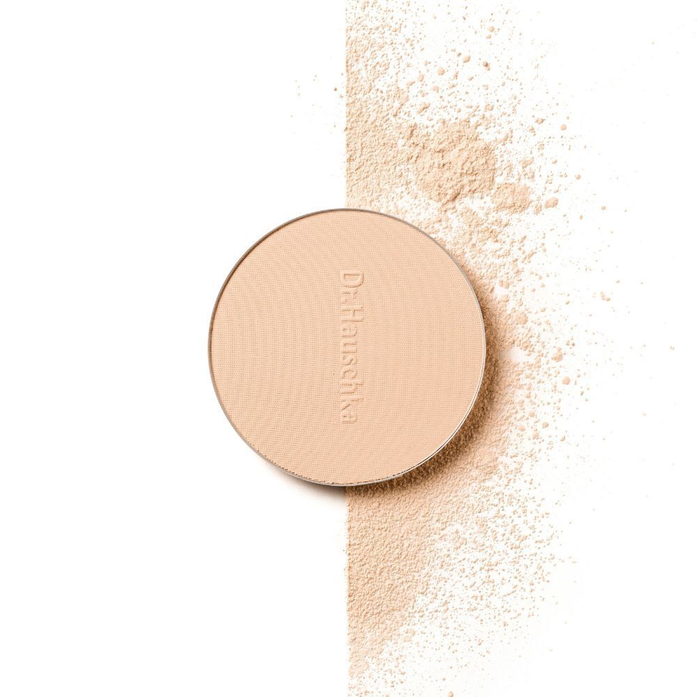 Cipria compatta Dr. Hauschka in astuccio scuro, con cipria sparsa accanto.