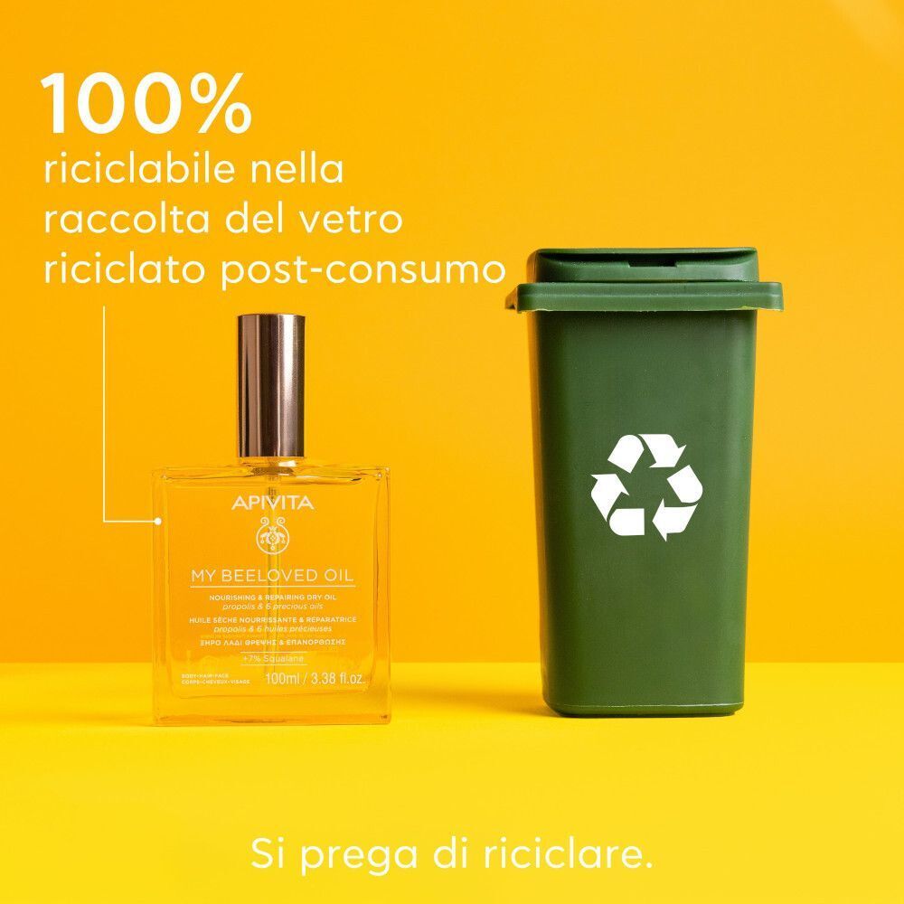 Flacone di APIVITA My Beeloved Oil accanto a un bidone di riciclaggio verde. Testo: '100% riciclabile nella raccolta del vetro riciclato post-consumo'.