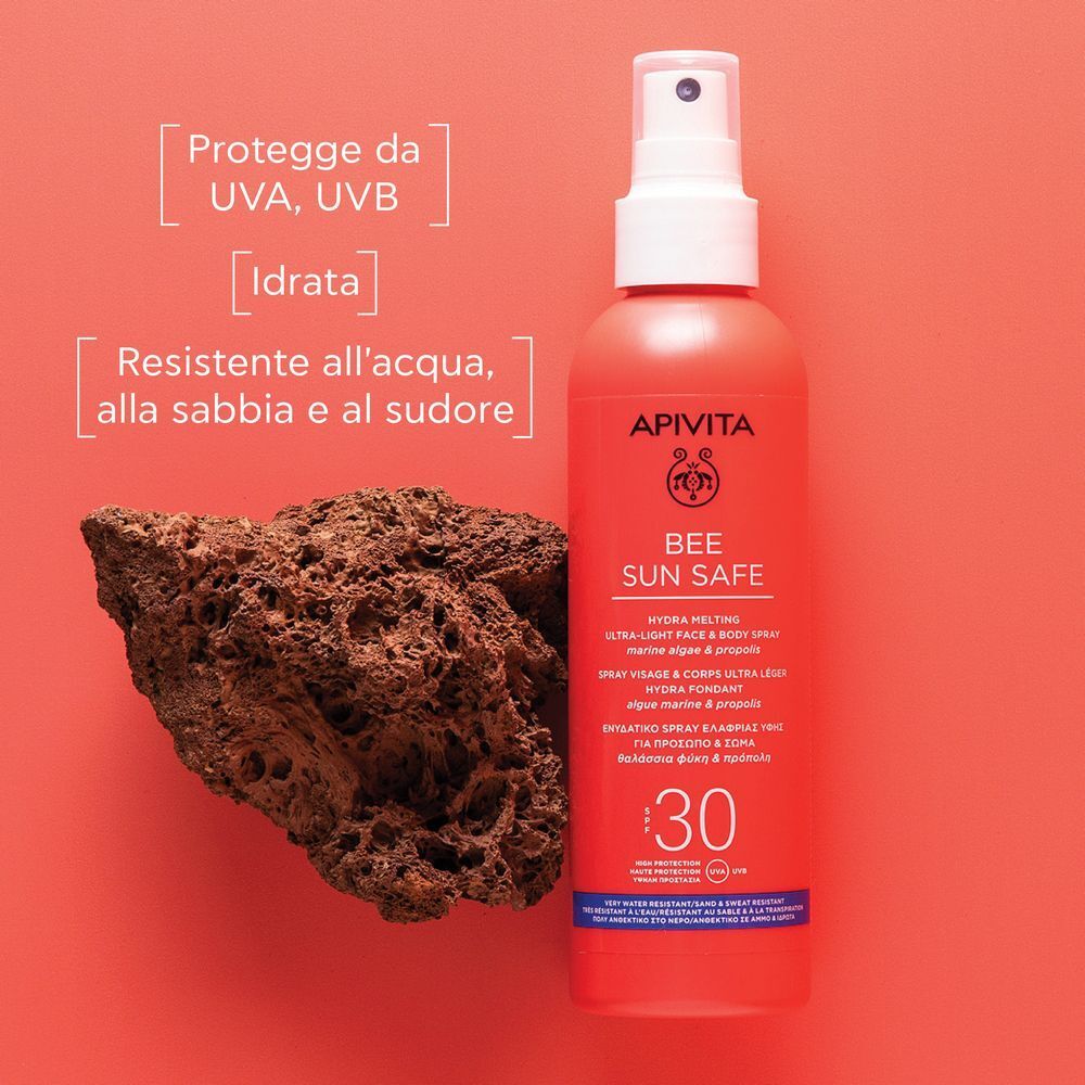 Flacone spray APIVITA Bee Sun Safe SPF 30 rosso accanto a un pezzo di roccia lavica.