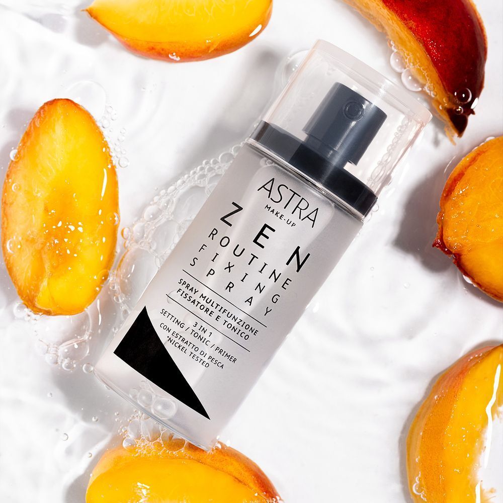 Spray fissante ASTRA Make-Up Zen Routine circondato da fette di pesca e acqua.