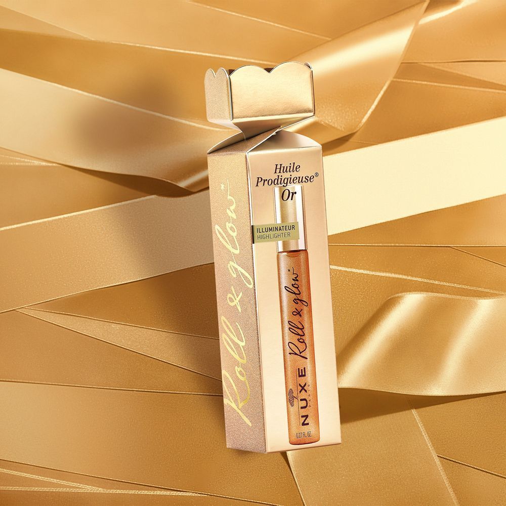 Un flaconcino roll-on Nuxe Huile Prodigieuse Or in confezione regalo dorata, circondato da nastri dorati.