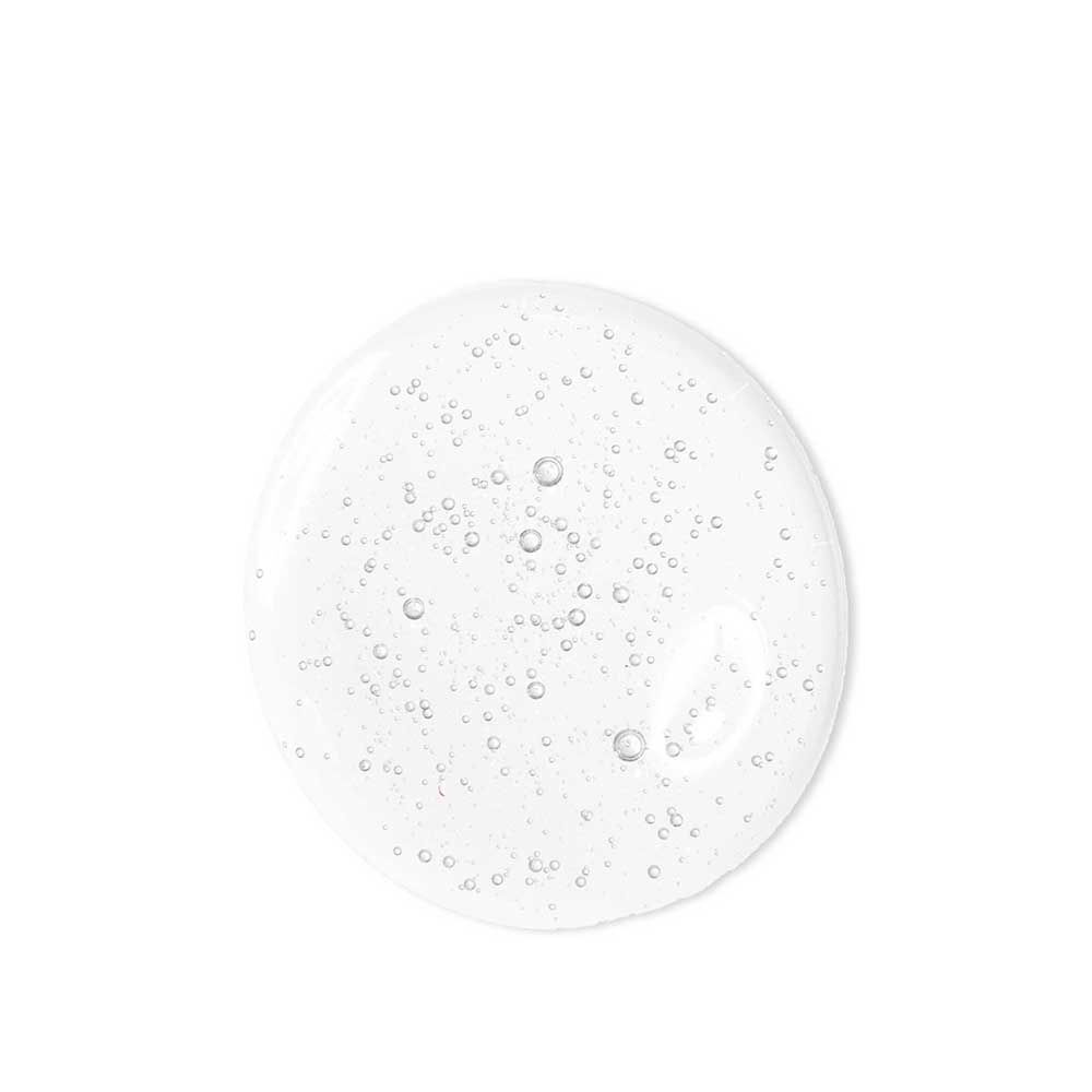 Una goccia di detergente viso trasparente con piccole bollicine d'aria su sfondo bianco.