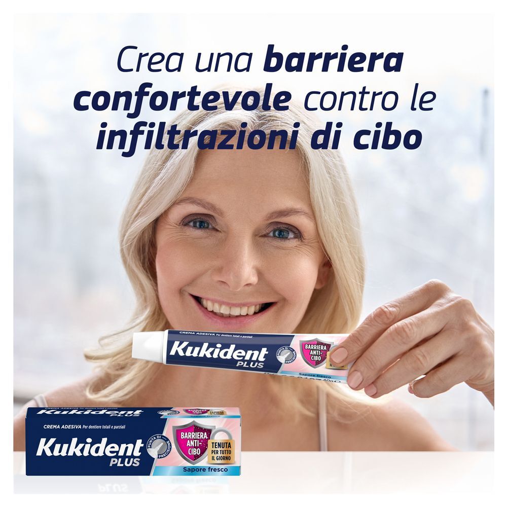 Donna tiene un tubetto di crema adesiva Kukident Plus. La confezione mostra una barriera anti-cibo.