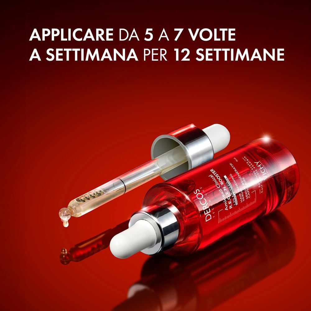Un flacone Vichy Dercos Aminexil con contagocce è appoggiato su una superficie rossa. Il contagocce trattiene una goccia di liquido.