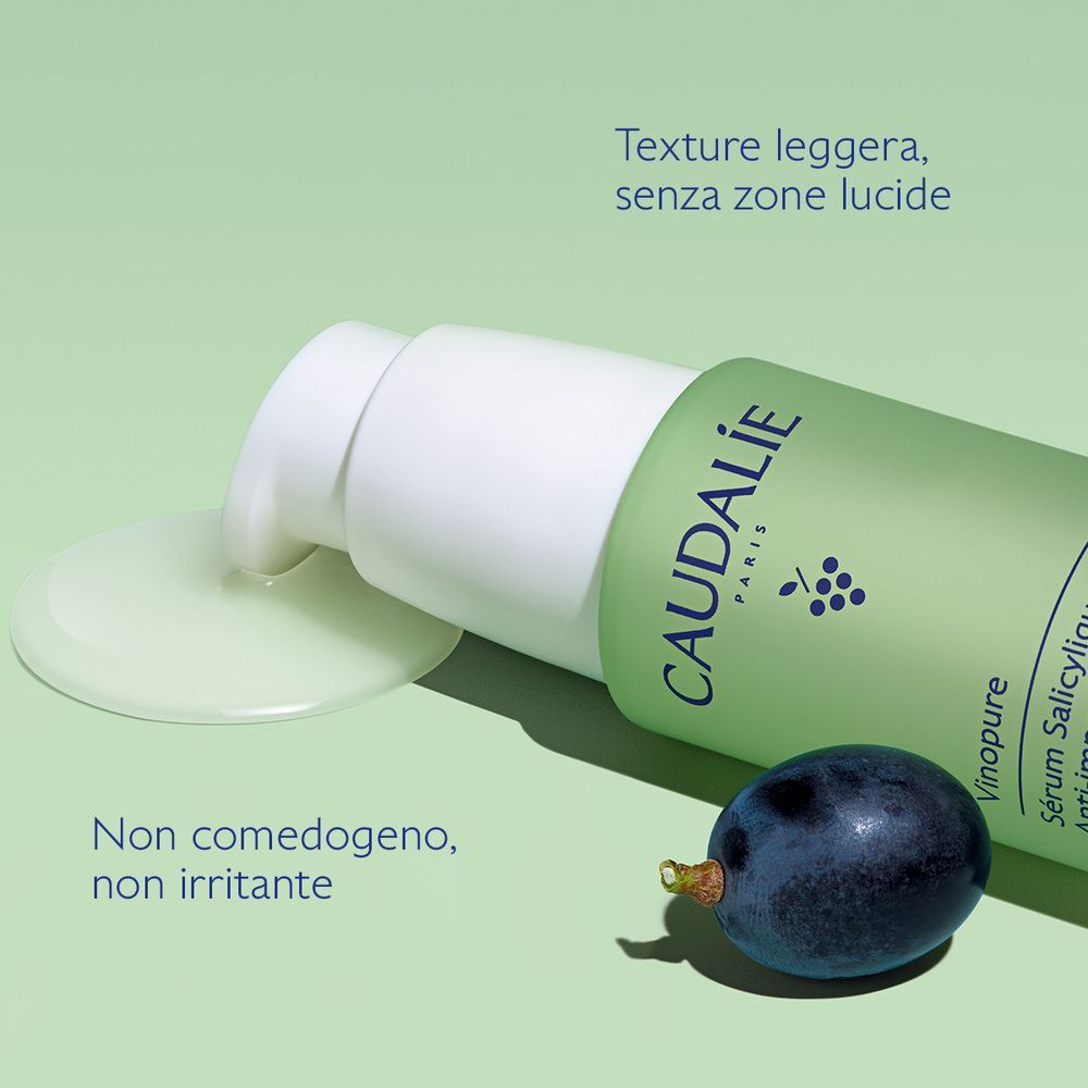 Siero Caudalie Vinopure con dispenser a pompa, una goccia di siero accanto, un'uva.
