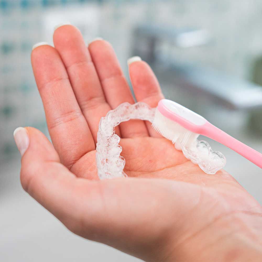 Mano che pulisce un apparecchio trasparente con uno spazzolino rosa.
