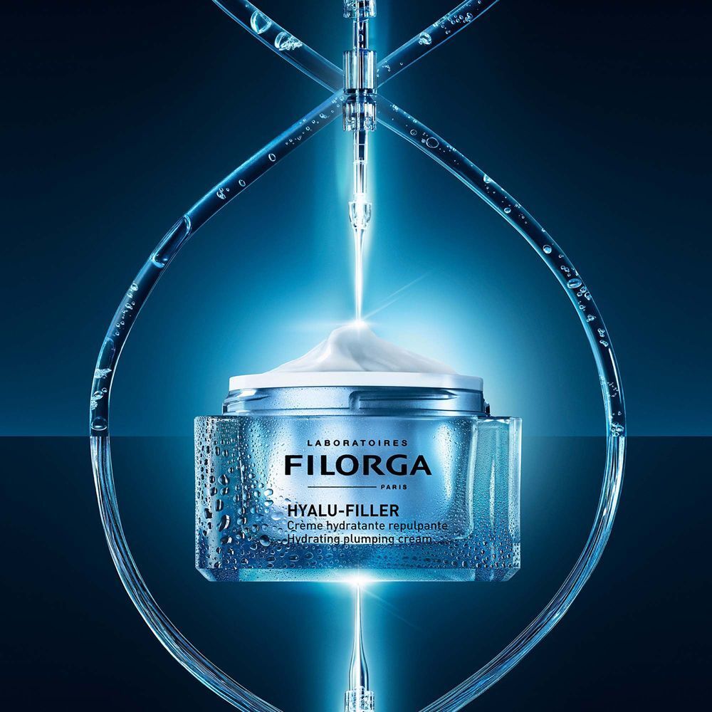 Crema idratante Filorga Hyalu-Filler in vasetto, circondata da gocce d'acqua e raggi luminosi blu.