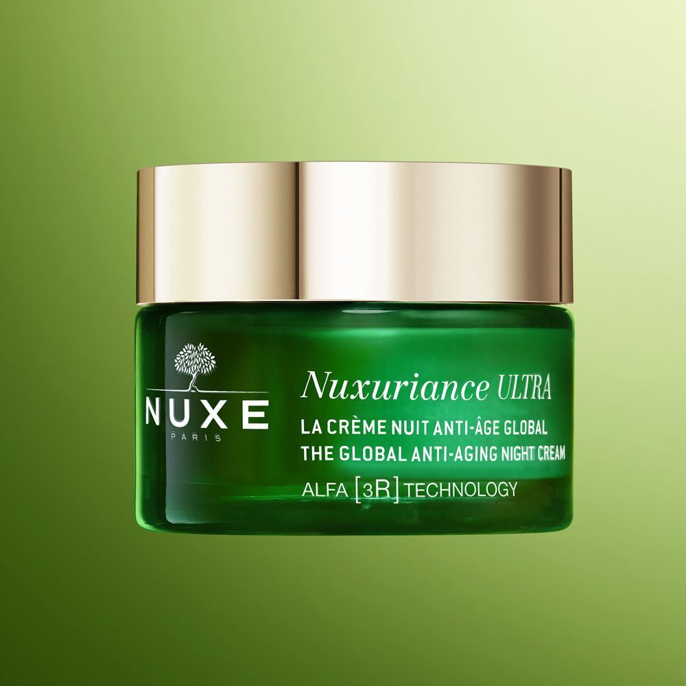 Un vasetto Nuxe Nuxuriance Ultra con tappo dorato su sfondo verde.