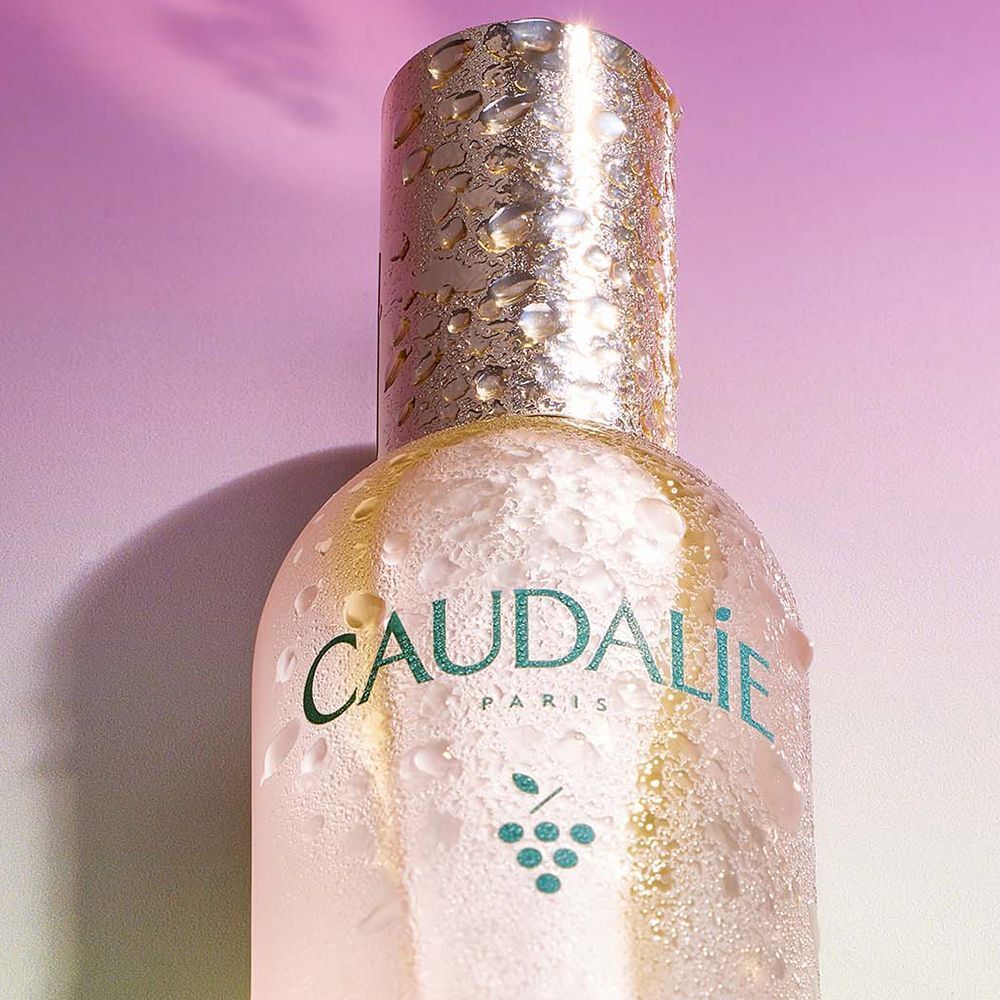 Primo piano del collo della bottiglia Caudalie Beauty Elixir con gocce d'acqua.